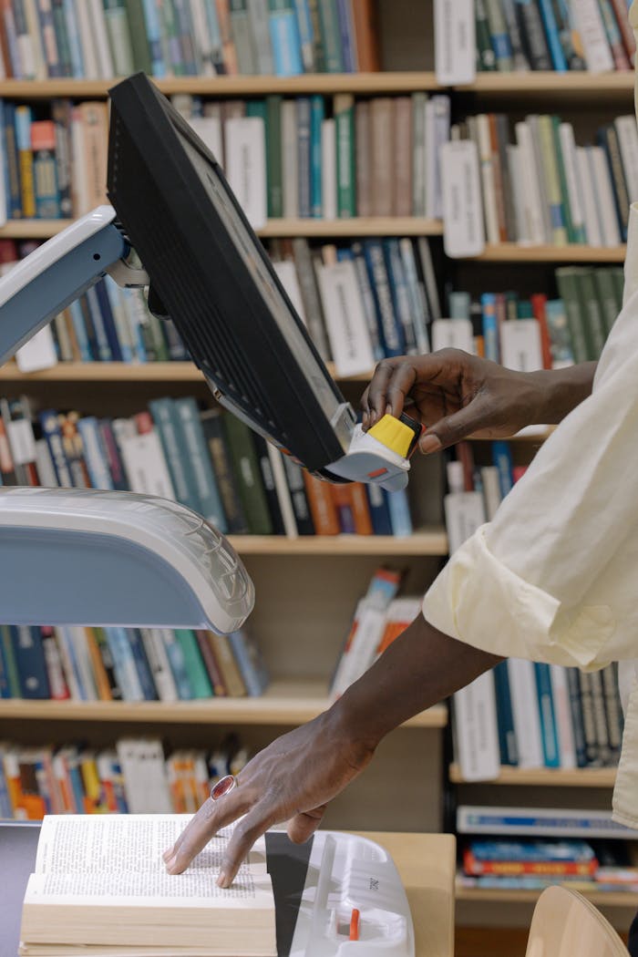 Hands scanning a textbook in a modern library, showcasing technology and learning resources.