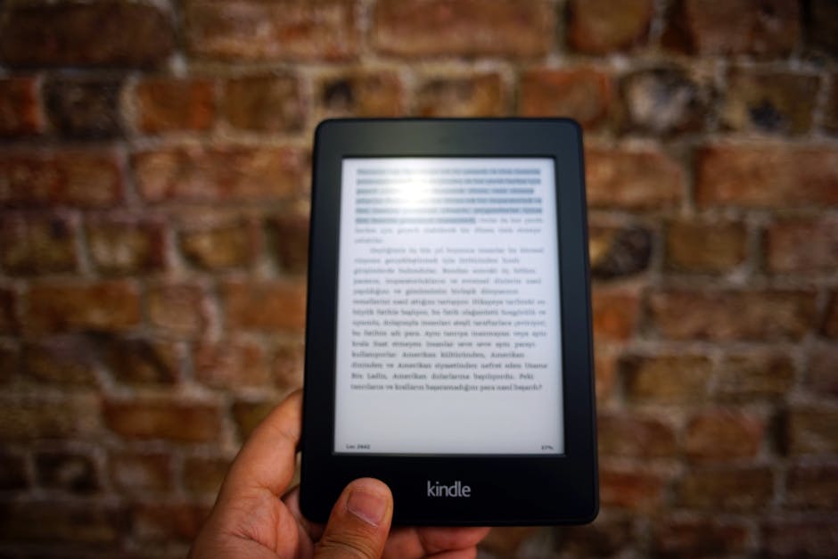 pexels photo 844734 844734 Close-up of a Kindle e-reader held by a person, showcasing a digital reading device against a textured brick wall backdrop.